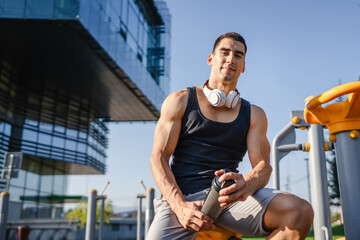 Wall Mural - One caucasian man young male athlete take a brake during outdoor training in the park outdoor gym hold supplement shaker in hand happy confident strong copy space