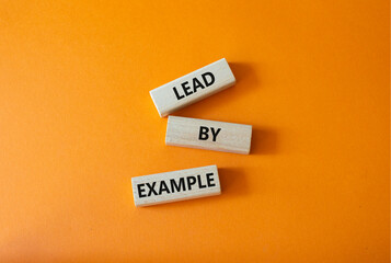 Lead by Example symbol. Concept word Lead by Example on wooden cubes. Beautiful orange background. Business and Lead by Example concept. Copy space.