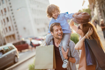 Young family with child on city street holding shopping bags