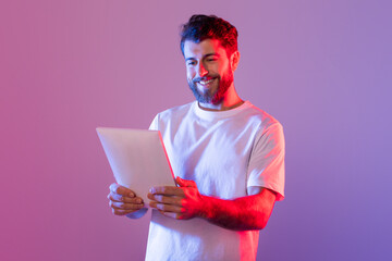 Leinwandbilder - A man wearing a white t-shirt is shown holding a tablet device in his hands. He appears focused on the screen, engaged in technology.