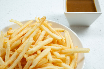 A view of a plate of french fries, and a square condiment cup of curry dip.