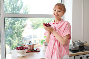 Poster - Beautiful young woman with bowl full of ripe cherries in kitchen near window