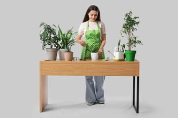 Poster - Young happy woman at table with gardening tools and houseplants on white background