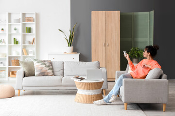 Poster - Young African-American woman turning on air conditioner at home