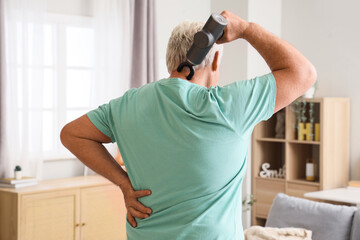 Poster - Mature man massaging his neck with percussive massager at home, back view