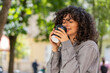 © Andrii Iemelianenko - Happy Caucasian young woman enjoying morning coffee hot drink and smiling outdoors. Relaxing, taking a break. Lady girl walking on urban city street drinking coffee to go. Town lifestyles. Sunny park