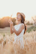 © Satori Studio - A woman is standing in a field of tall grass, holding a bunch of wheat in her hands. She is smiling and she is enjoying the moment. Concept of peace and happiness