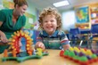 © evgenia_lo - A Caucasian boy with curly hair laughing while playing with a colorful toy in a preschool setting, with a woman assisting him.