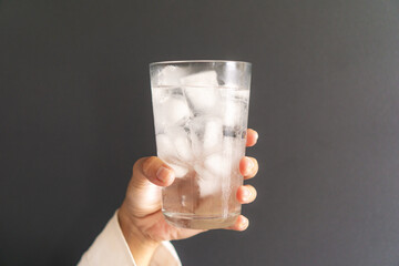 woman holding a glass of cold water with ice cubes, dark gray backround