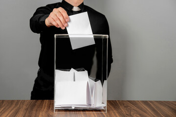 Wall Mural - A pastor voter casting a ballot into a ballot box on election day. Referendum, democracy, religion and politics concept