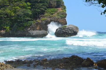 waves hitting two large rocks on the beach in sunny weather