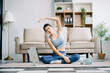 © Nuttapong punna - Asian Woman Doing Yoga and Watching Online Tutorials on Laptop, Training in Living Room at home