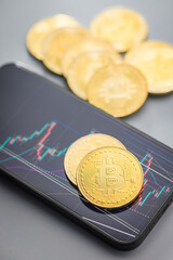 Bitcoin gold coin on gray background. Cryptocurrency and business chart in cellphone.