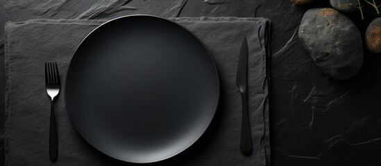 Poster - A table with a dark stone surface showcasing an empty black plate surrounded by a white napkin This copy space image is suitable for a food background menu or recipe It depicts a table setting captur