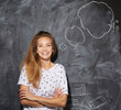 © Westend61 - Smiling woman with arms crossed in front of thought bubble on chalkboard
