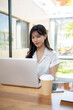 © bongkarn - A beautiful Asian businesswoman focusing on her work on a laptop computer in a cafe co-working space
