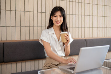 Businesswoman is smiling at the camera with a coffee cup in her hand while working remotely in cafe.