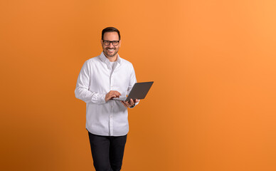 Portrait of confident businessman doing online research over wireless computer on orange background