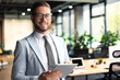 © ty - Modern business man in formalwear using digital tablet while standing near window in the office