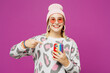 © ViDi Studio - Young happy lesbian woman wear pink animal clothes hold in hand use point index finger on mobile cell phone isolated on plain purple background studio portrait Pride day June month love LGBTQ concept