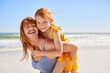 © Rido - Happy young mother giving daughter a piggyback ride at beach