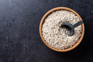 Poster - Rolled oats, healthy breakfast cereal oat flakes in bowl on black slate background. Top view. Copy space