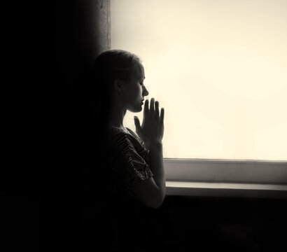 Young girl prays at the window