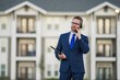 © Volodymyr - Real estate agent business man in suit hold holder clipboards and talking on phone. Businessman. Business Man broker or real estate agent. Business man in suit outdoor. Real estate business man.