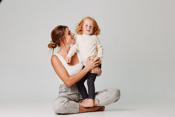 Wall Mural - Mother and daughter sit on floor in front of white background, family time together, home lifestyle and love concept