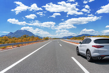 a white car drives along the highway against the backdrop of rocky mountains on a sunny day.
