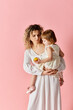 © LIGHTFIELD STUDIOS - Woman holding child in white dress on pink background.