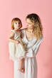 © LIGHTFIELD STUDIOS - A mother holding her little girl in a white dress on a pink background.