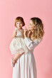 © LIGHTFIELD STUDIOS - A woman in a white dress cradles a little girl in a pink background.