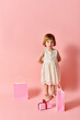 © LIGHTFIELD STUDIOS - Adorable girl in white dress with gift bags against pink backdrop.