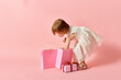 © LIGHTFIELD STUDIOS - Adorable girl in white dress holding pink shopping bags against a pink background.