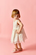 © LIGHTFIELD STUDIOS - Little girl in white dress standing on pink backdrop.