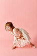 © LIGHTFIELD STUDIOS - A little girl in a white dress stands charmingly against a pink backdrop.