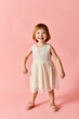 © LIGHTFIELD STUDIOS - Adorable child wearing white dress, standing on pink background.