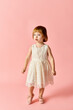 © LIGHTFIELD STUDIOS - A cute girl in a white dress stands gracefully against a vibrant pink background.