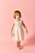 © LIGHTFIELD STUDIOS - Little girl in white dress stands gracefully against pink backdrop.