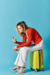 © LIGHTFIELD STUDIOS - A woman sits atop a yellow suitcase, engrossed in her phone.