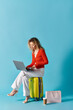 © LIGHTFIELD STUDIOS - Woman sitting on a suitcase, using a laptop.