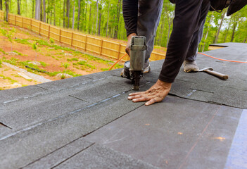 Wall Mural - In roofer uses an air pneumatic nail gun to install new asphalt bitumen shingles