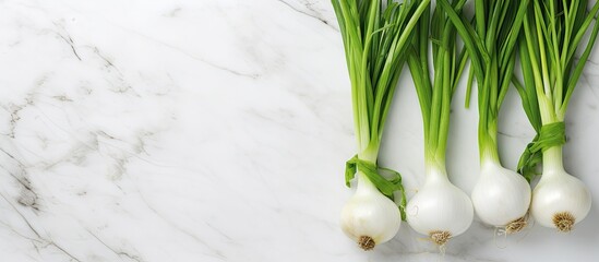Poster - A cluster of fresh green spring onions arranged on a white marble surface captured from above This flat lay composition offers ample space for adding text
