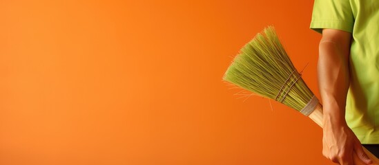 Fototapete - Closeup of a man holding a green broom against an orange backdrop The image provides ample space for text