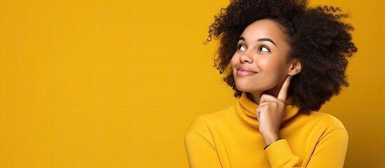 Poster - A pensive African American girl with a smile looks at the copy space image beside her on a yellow studio background She contemplates a good promotion deal representing an advertising concept for happy
