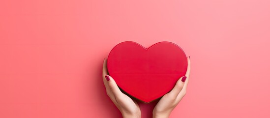 Poster - A heart shaped closed red box is held by female hands on a pink background It creates a festive backdrop with copy space