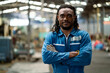© KANGWANS - A man in a blue uniform stands in a factory with his arms crossed. He has a serious expression on his face