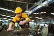 © KANGWANS - A man in a yellow and blue uniform is working on a machine. He is wearing a yellow helmet and a yellow shirt