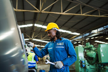 Wall Mural - A man in a blue jumpsuit is working on a machine. He is wearing a yellow helmet and gloves